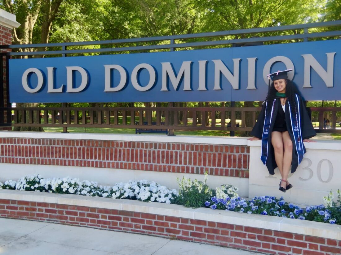 Student in graduation gown sitting in front of Old Dominion sign